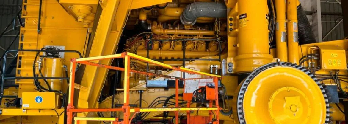 Plataforma elevadora frente a maquinaria pesada amarilla en mantención dentro de taller industrial.