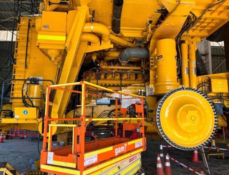 Plataforma elevadora frente a maquinaria pesada amarilla en mantención dentro de taller industrial.